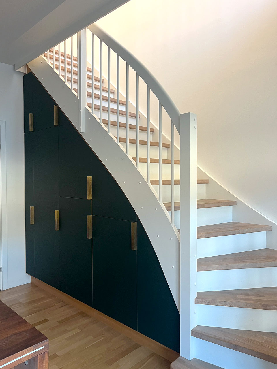 Skræddersyet køkkenopbevaring under trappe i grøn Forbo linoleum og egetræ – set op ad trappen med alle låger og messinggreb, Nordvest KBH