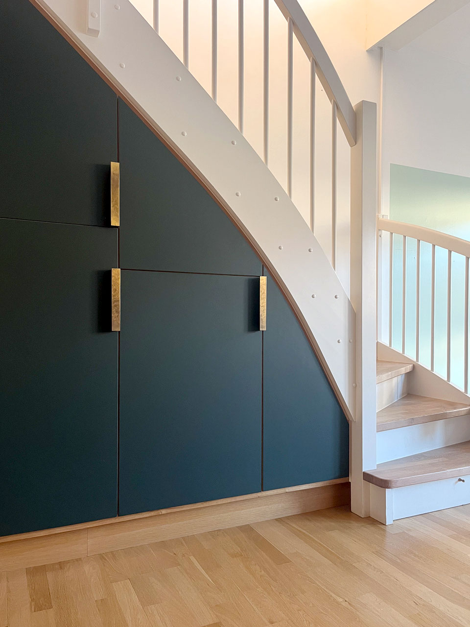 Nederste del af køkkenopbevaring under trappe: her gemmer sig fryser, store grydeskuffer og hylder bag grønne linoleumslåger.