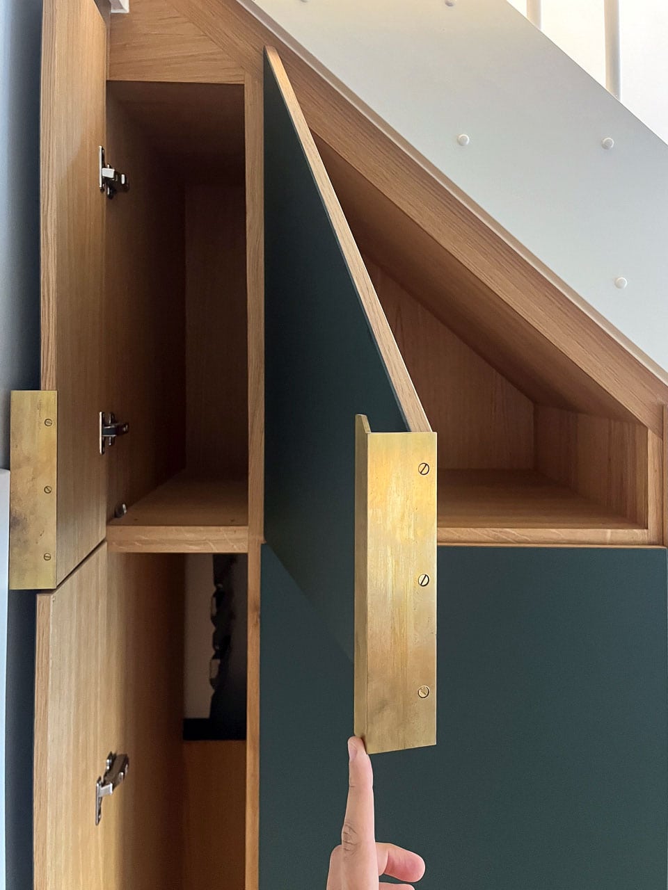 Øverste del af opbevaring under trappe: tre åbne grønne linoleumslåger med håndlavede messinggreb og ligkavede messingskruer – pladsen udnyttet helt op til loftet