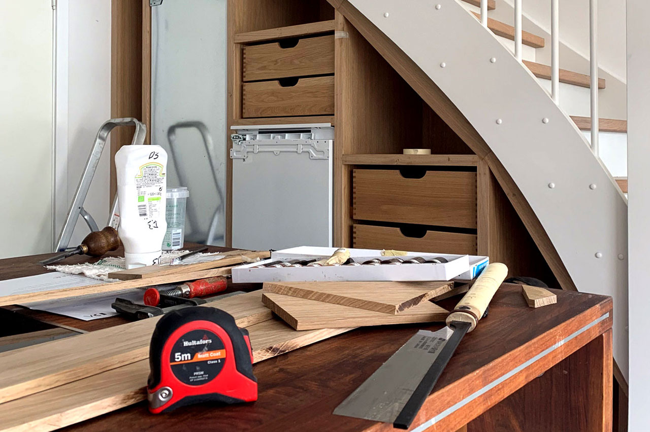 Work-in-progress: indbygget køkkenopbevaring under trappe før montering af linoleumslåger – fryser, skuffer og køleskab synlige i baggrunden