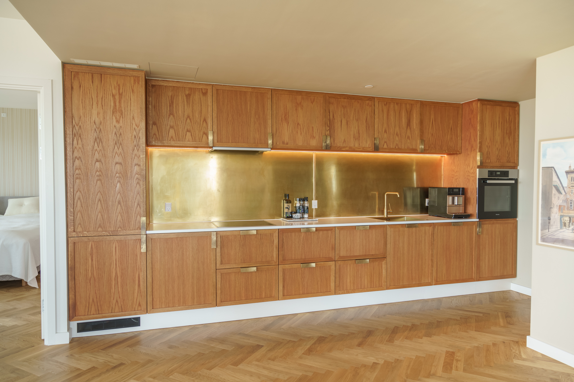 Fuldt overblik forfra – alle 6 overskabe, Højsakbe på hver side, top belyst messingbagplade, Miele ovn og Corian bordplade